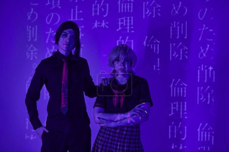 modern cosplayers in students uniform looking at camera in vibrant blue neon light with hieroglyphs