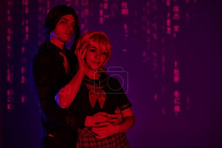 trendiger Mann umarmt Frau im Anime-Stil in Studentenuniform in rotem Neonlicht vor lila Hintergrund
