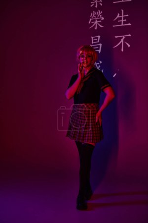 mujer sonriente en uniforme escolar en luz de neón sobre fondo púrpura con jeroglíficos, cosplayer