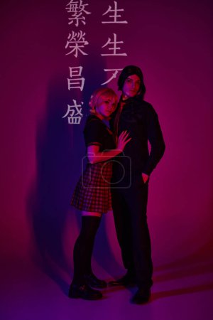 Photo for Couple of students in uniform in neon light on purple backdrop with hieroglyphs, trendy cosplayers - Royalty Free Image