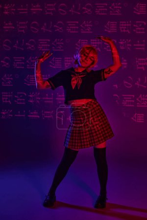 Photo for Tattooed anime woman in school uniform posing on neon purple backdrop with hieroglyphs projection - Royalty Free Image