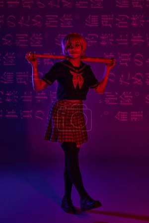 Photo for Trendy cosplay woman in school uniform with baseball bat on neon purple backdrop with hieroglyphs - Royalty Free Image