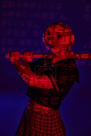 Photo for Anime woman in school uniform posing with baseball bat in neon light with hieroglyphs on blue - Royalty Free Image