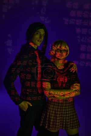 Photo for Anime style students in colorful neon projection of hieroglyphs on blue indigo backdrop, cosplayers - Royalty Free Image