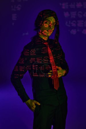 student in black wig and uniform looking at camera in neon light with hieroglyphs on blue  backdrop