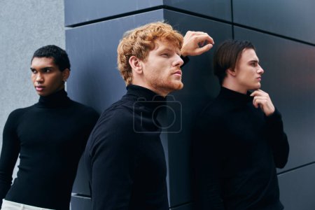 attractive pensive men in stylish black turtlenecks posing and looking away with wall backdrop