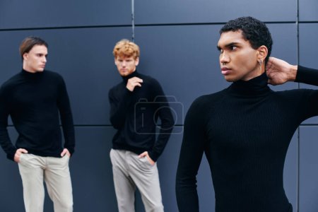 three multiracial young men in elegant casual outfits standing by the wall, fashion concept