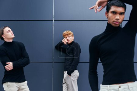 gut aussehende interrassische Gruppe von Männern posiert neben der Wand in lässigen schwarzen Rollkragenpullovern, Mode