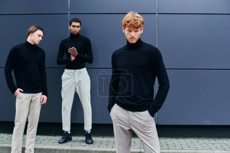 guapos hombres elegantes en cuellos altos negros con accesorios posando por la pared exterior, concepto de moda