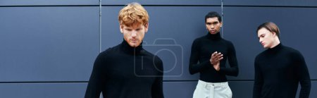 atractivos hombres jóvenes en cuellos altos negros con accesorios posando por la pared exterior, moda, pancarta