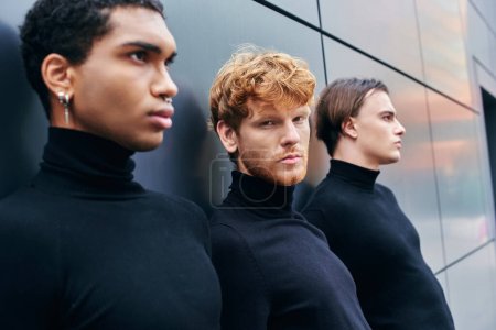 multiethnic elegant men in turtlenecks posing shoulder to shoulder standing by wall, fashion concept
