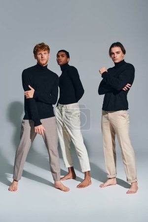 drei verschiedene stylische Männer in eleganten Anzügen stehen und blicken vor grauem Hintergrund in die Kamera