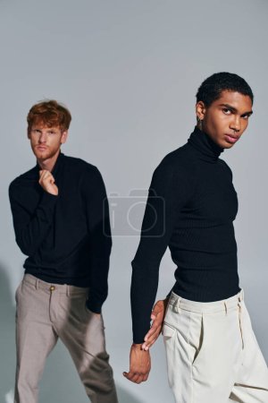 vertical shot of two multicultural men in black elegant turtlenecks looking at camera, fashion