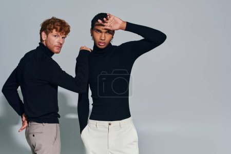red haired man with his hand on shoulder of african american man in black turtlenecks, fashion