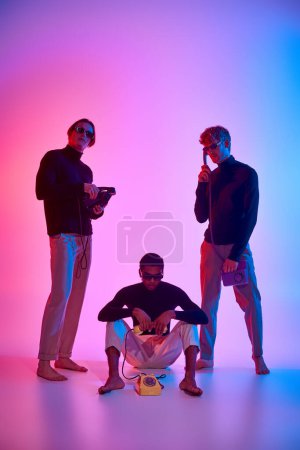vertical shot of young multicultural men posing with landline phones surrounded by neon lights
