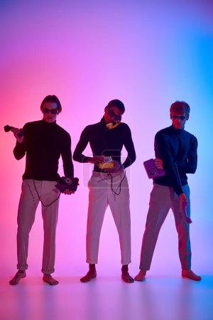 Téléchargez les photos : Beaux modèles masculins multiethniques entourés de néons posant avec des téléphones fixes, hommes puissance - en image libre de droit