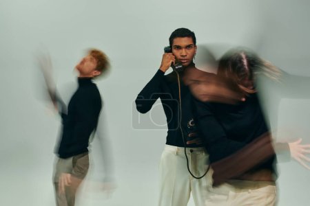 junger afrikanisch-amerikanischer Mann posiert mit Festnetztelefon mit anderen männlichen Models in Bewegung, Langzeitbelichtung