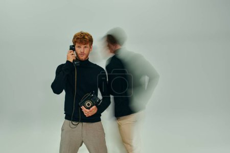 red haired man in elegant turtleneck with landline phone with other man moving, long exposure