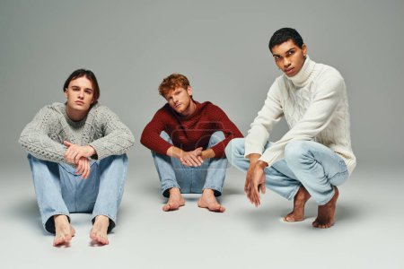 good looking interracial men in casual outfits posing on floor and looking at camera, fashion