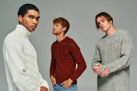 good looking diverse men in warm casual sweaters posing in motion on gray backdrop, fashion concept