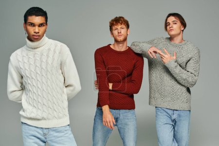 junges multiethnisches Trio in lässigen Pullovern und Jeans posierend und in die Kamera blickend, Männerpower