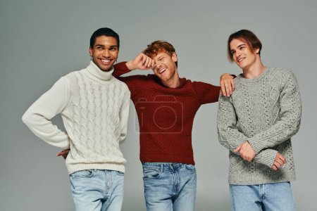 cheerful diverse male models in casual sweaters laughing and posing on gray backdrop, men power