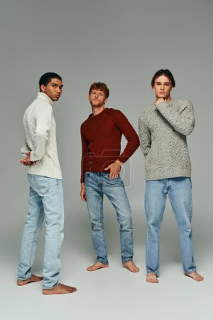 Photo for Vertical shot of young diverse friends in casual attires posing on gray backdrop, men power - Royalty Free Image