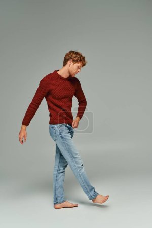 Photo for Handsome appealing bearded man in warm sweater walking barefoot on gray backdrop, fashion concept - Royalty Free Image