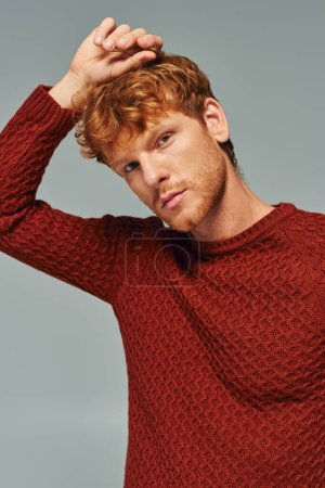 portrait of young red haired man in red comfy sweater posing and looking at camera, fashion