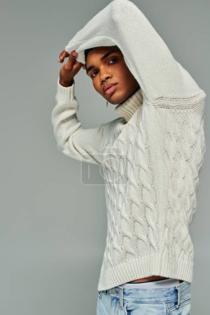 schöner junger afrikanisch-amerikanischer Mann in stylischem Pullover posiert mit erhobenen Armen, Modekonzept