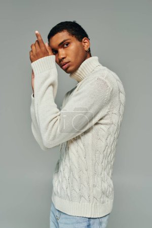 atractivo hombre afroamericano en suéter blanco posando con las manos cerca de la cara mirando a la cámara