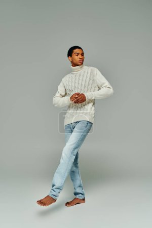 schöner stylischer afrikanisch-amerikanischer Mann in warmem Pullover und Jeans, der wegschaut, Modekonzept