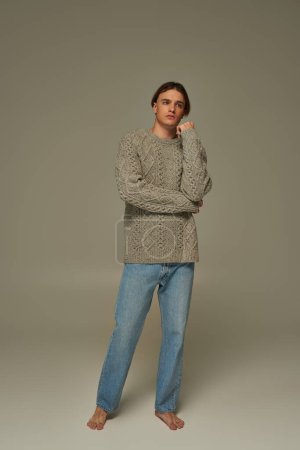 attractive elegant man in stylish cozy sweater and jeans posing with hand near face and looking away