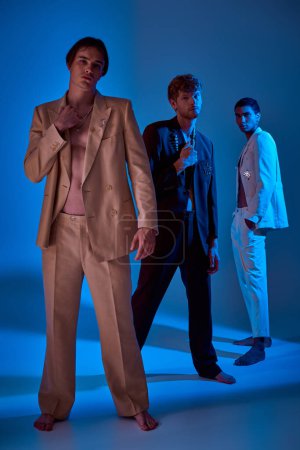vertical shot of young stylish male models in elegant suits with accessories, blue lights, men power