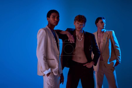 handsome diverse men posing actively in elegant suits with accessories on blue backdrop, fashion