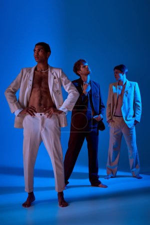 vertikale Aufnahme eines afrikanisch-amerikanischen Mannes im aufgeknöpften Anzug mit anderen männlichen Models, die vor dem Hintergrund posieren