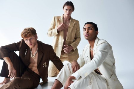three young multiethnic male models in elegant suits posing on floor looking at camera, men power