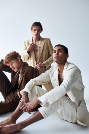 good looking diverse men in elegant suits with accessories posing on floor, fashion concept