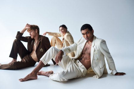 handsome multicultural male models in classy suits posing on floor with gray backdrop, men power