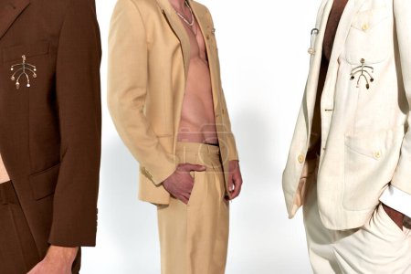 vista recortada de tres hombres jóvenes multiétnicos en trajes elegantes desabotonados sobre fondo gris, moda
