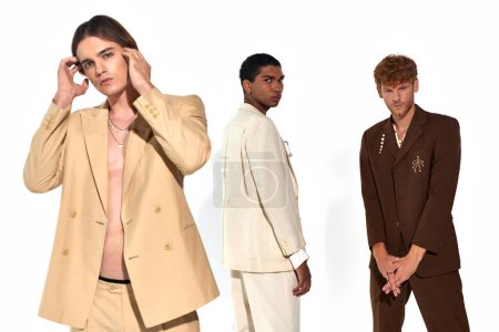 drei stylische multikulturelle Männer in lebendigen Anzügen mit Accessoires posieren auf weißem Hintergrund