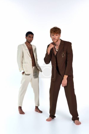 gut aussehende elegante Männer in Anzügen posieren munter vor weißem Hintergrund, schauen in die Kamera, Mode