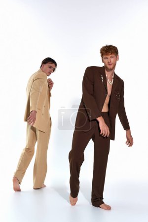 zwei gut aussehende junge männliche Models in edlen Anzügen posieren in Bewegung vor weißem Hintergrund, Männer-Power