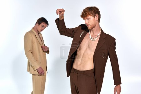 young red haired man in suit with accessories with other male model on backdrop, men power