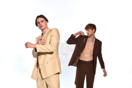 handsome young man in beige suit posing with other male model in unbuttoned suit, men power
