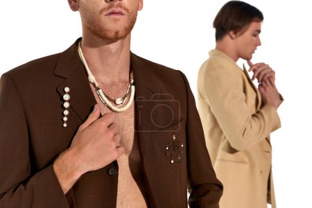 cropped view of stylish young man in unbuttoned suit with other man on blurred backdrop, men power