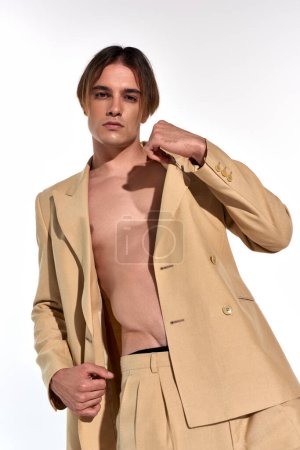 vertical shot of appealing young male model in unbuttoned suit posing alluringly on white backdrop