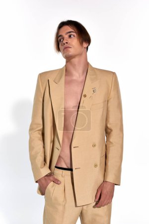 vertical shot of handsome attractive male model in beige sexy suit posing on white backdrop, fashion
