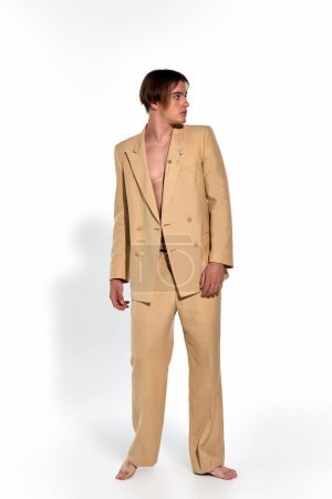 vertical shot of good looking stylish male model in beige suit posing barefoot and looking away