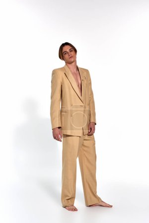 tiro vertical de atractivo hombre sexy en traje elegante beige de pie y mirando a la cámara, la moda